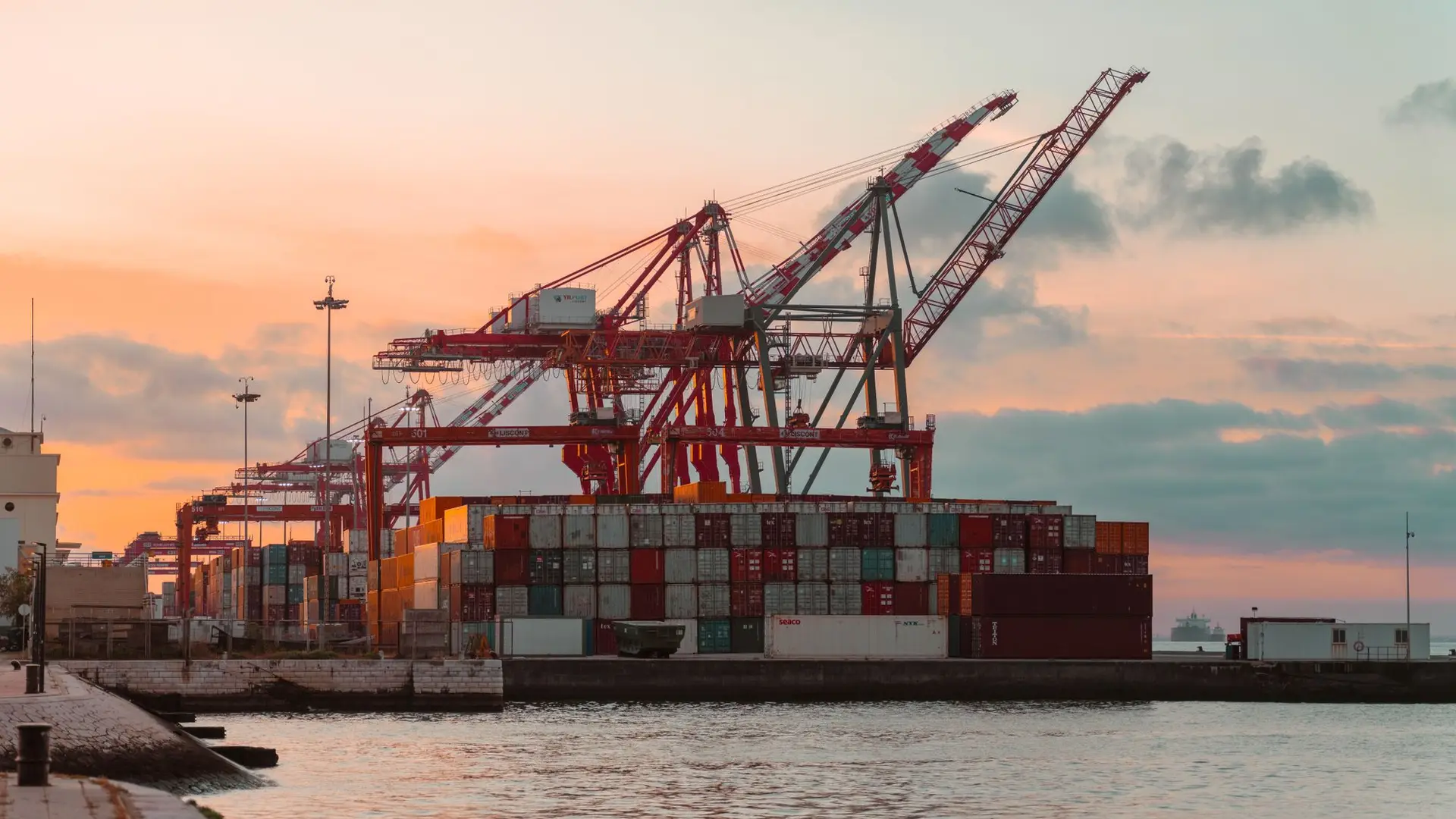 Container cranes loading a cargo vessel at a port during sunset