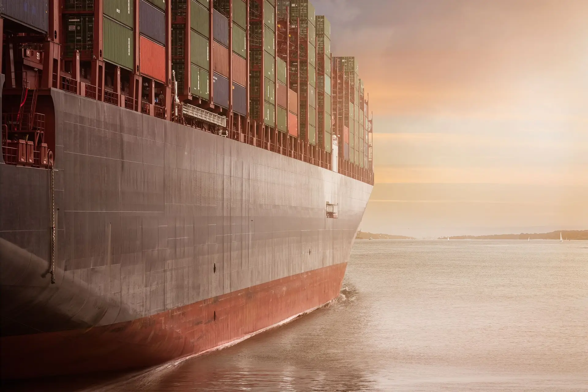 A large cargo ship loaded with containers sailing under a vibrant sunset sky