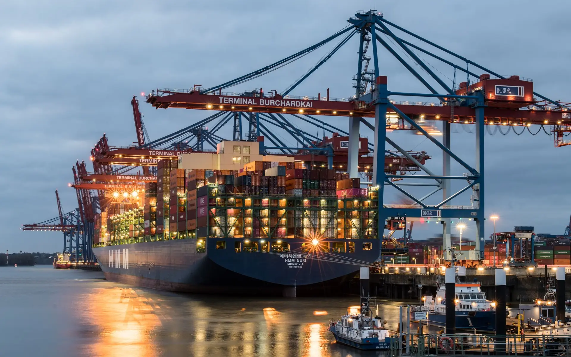 Container ships moored at a busy port terminal at dusk, cranes silhouetted against the sky