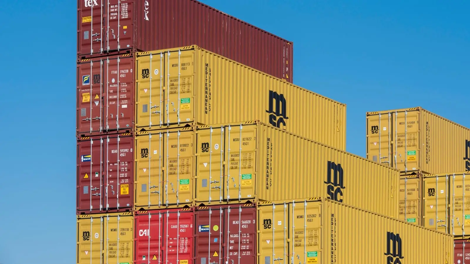 Shipping containers stacked several high against a clear blue sky